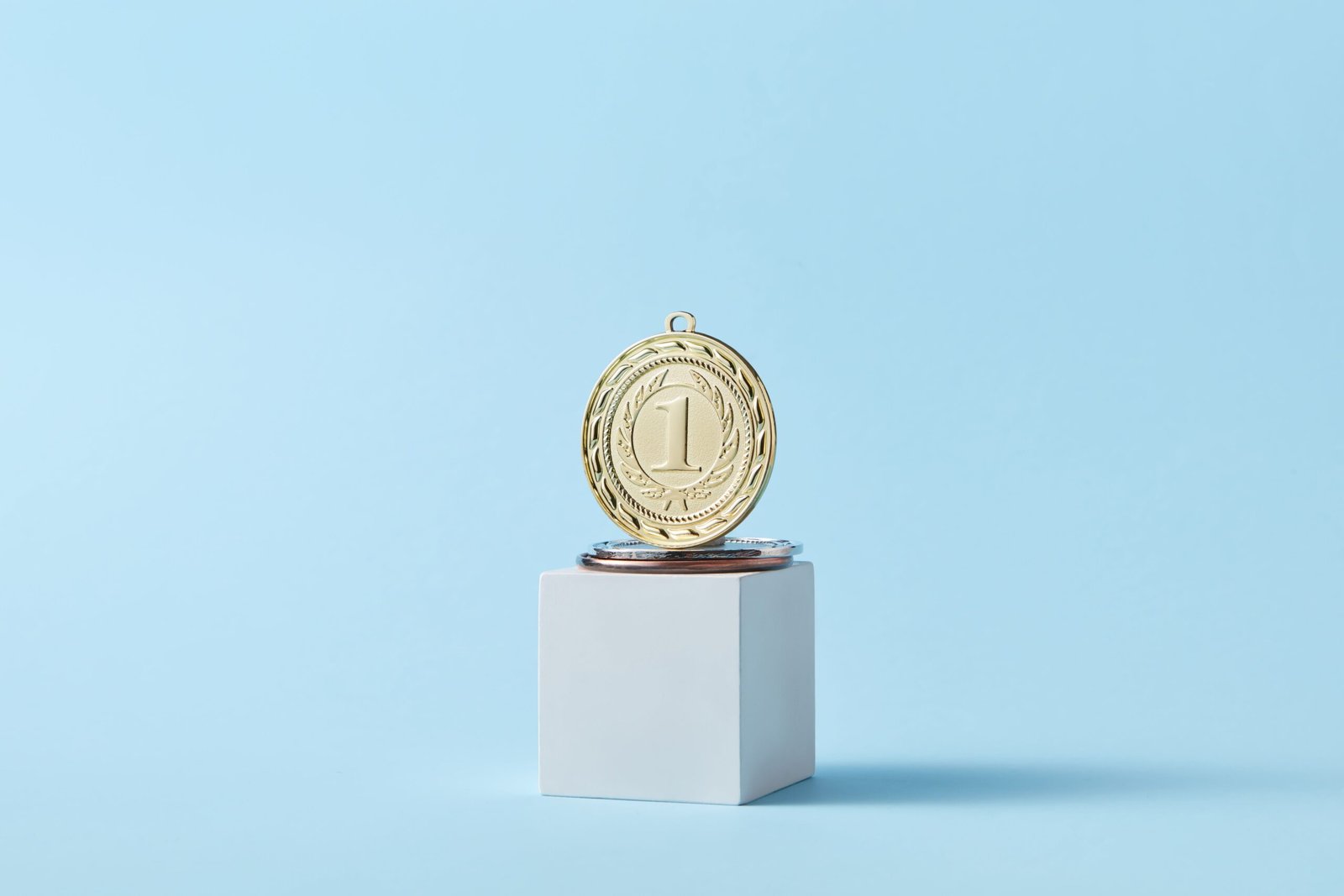 Close-up of a gold medal on a podium with a baby blue background, symbolizing victory.
